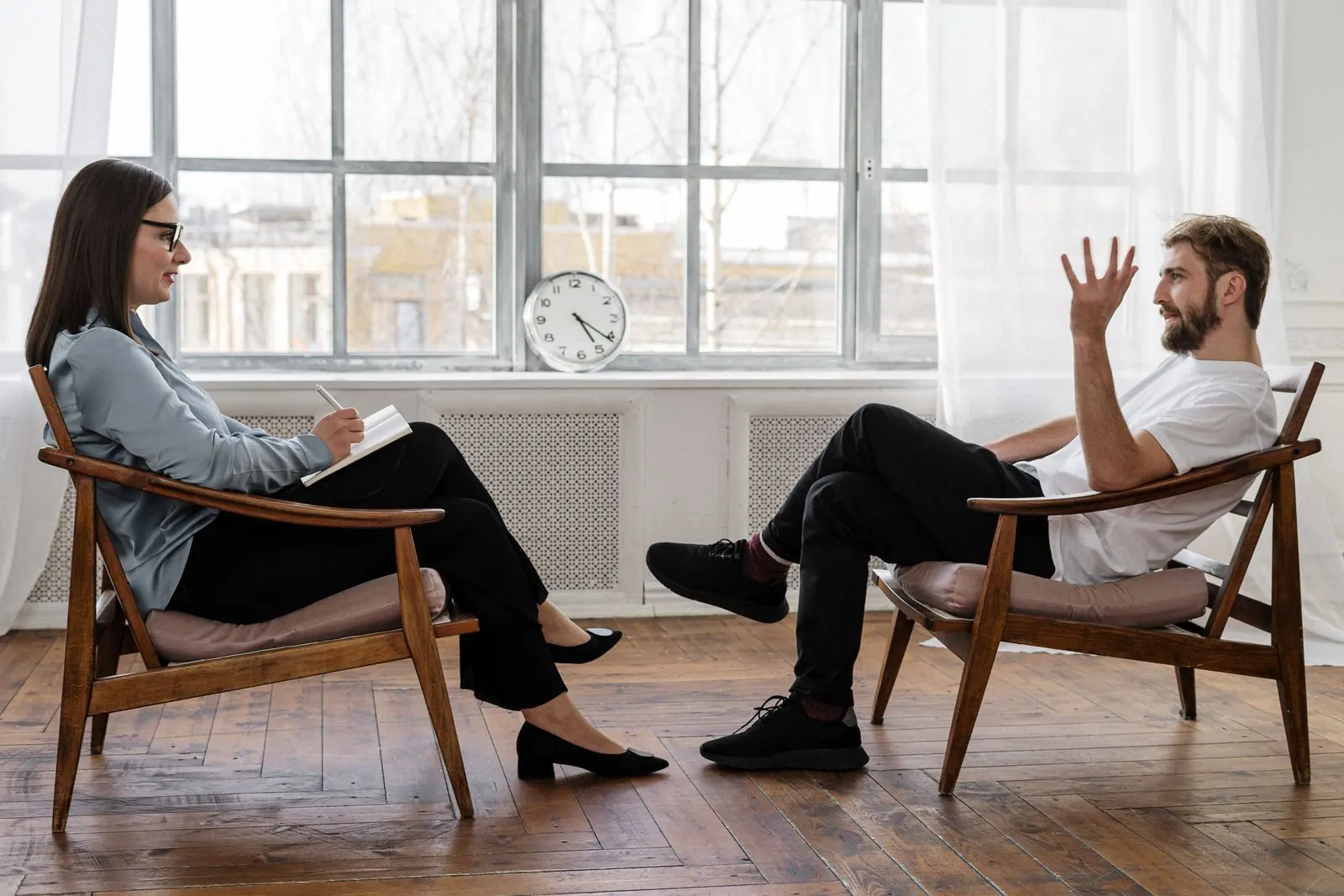 Two people sitting across from each other in a bright room, talking through a conversation.
